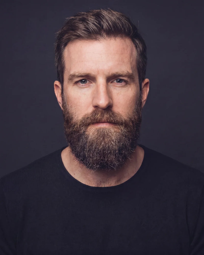 Man with a beard wearing a black shirt against a dark background