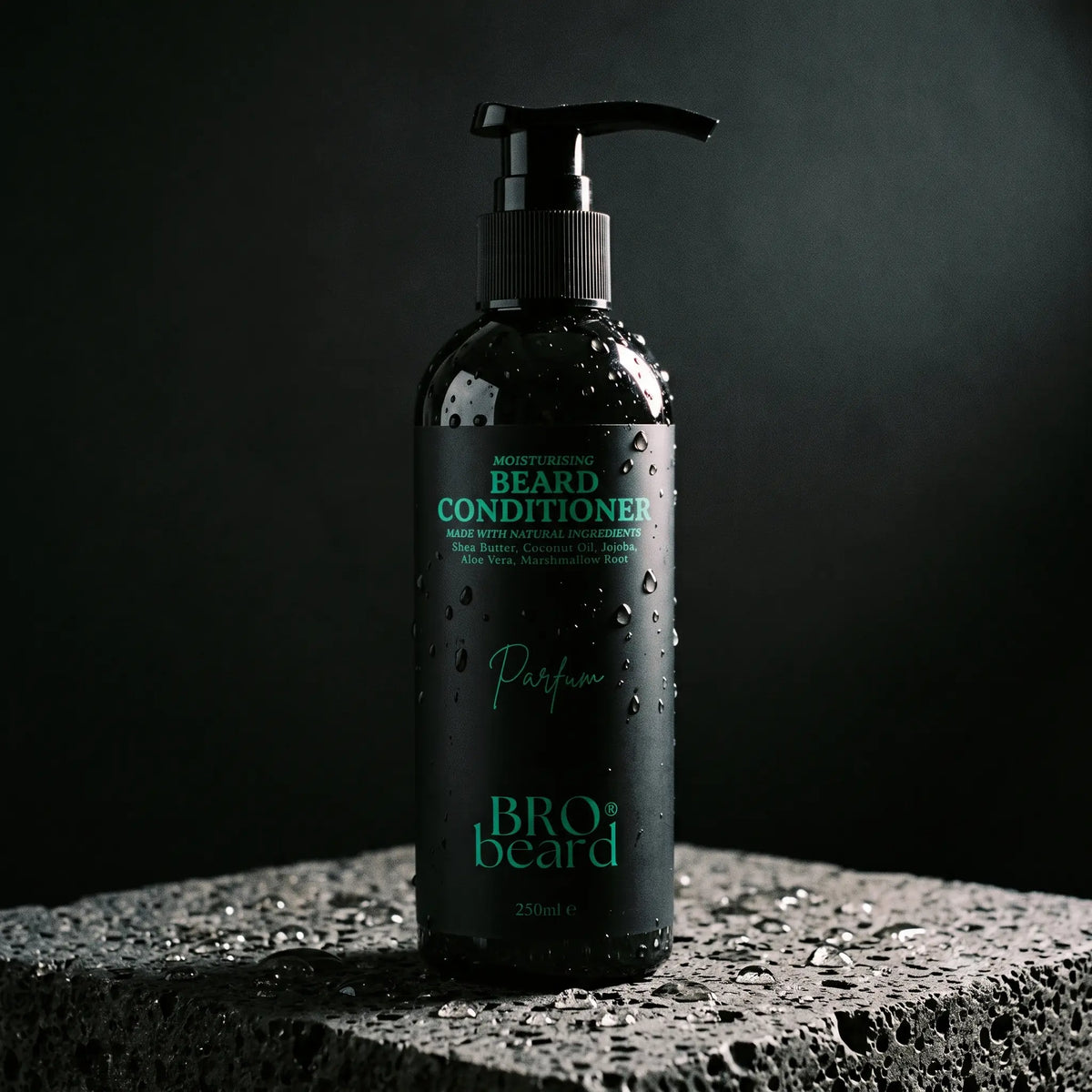 A black pump bottle of Bro Beard Beard Conditioner with green text, covered in water droplets, standing on a textured stone surface against a dark background.