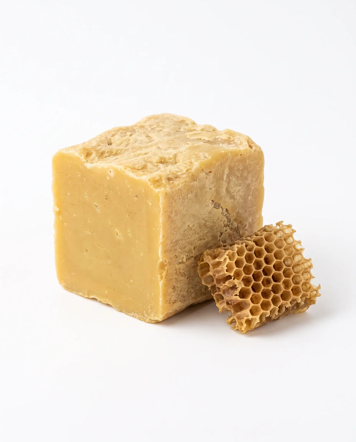 A rectangular block of pale golden honey with a natural honeycomb piece resting against it, photographed on a clean white background.