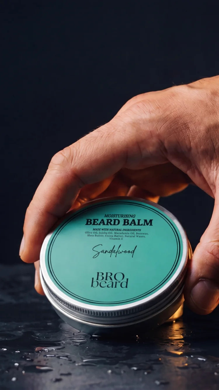 Hand holding a jar of Bro Beard sandalwood beard balm against a dark background
