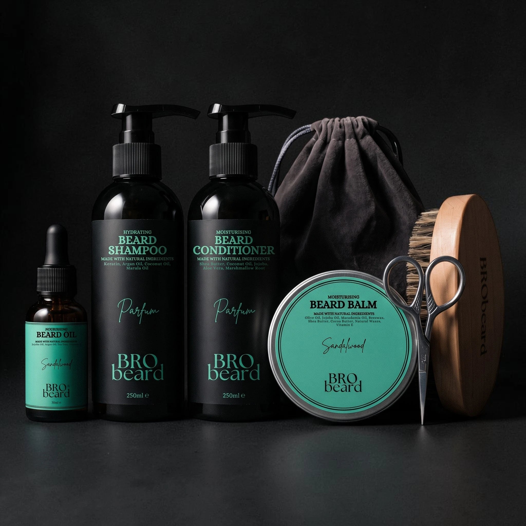 A beard grooming kit by BRO Beard arranged on a dark studio background, including a small dropper bottle, two pump bottles of beard shampoo and conditioner, a round tin of beard balm, a wooden brush, metal scissors, and a dark drawstring pouch.