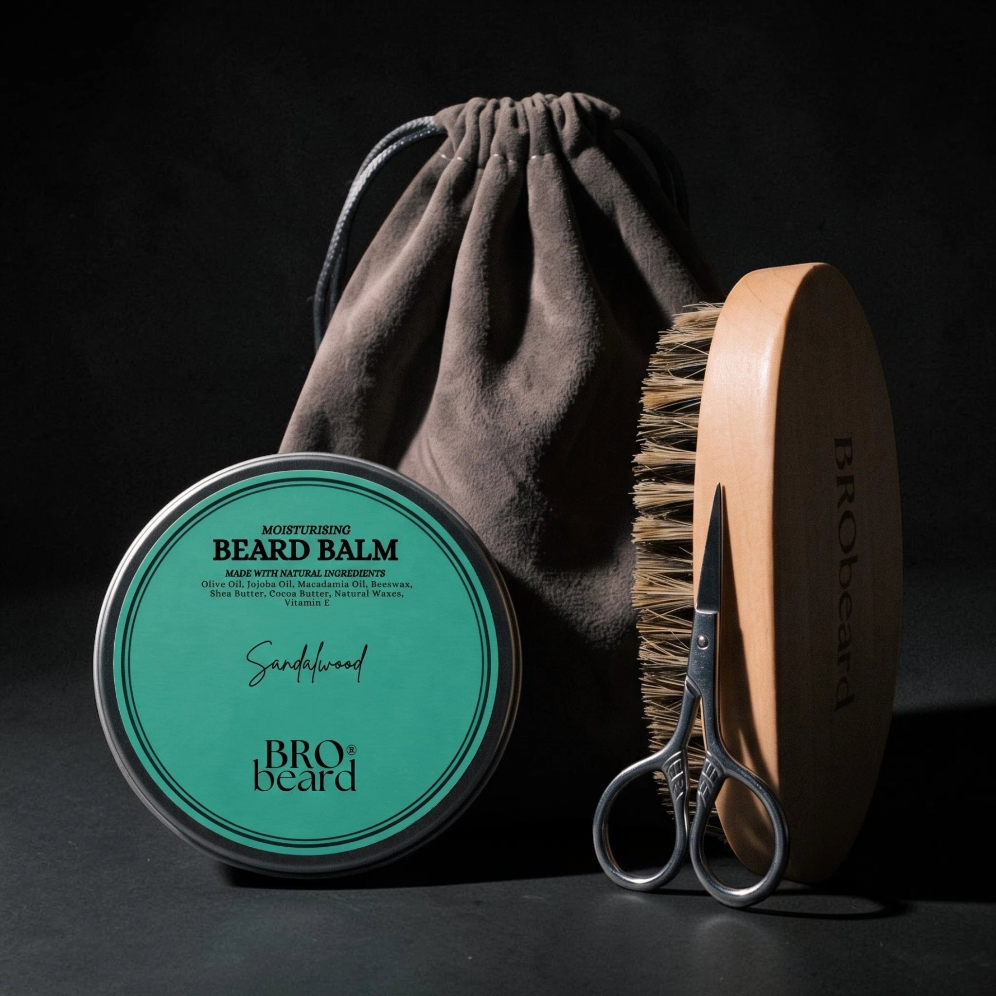 Bro beard beard care set including a round tin of Sandalwood beard balm, a wooden-handled brush, silver scissors, and a dark brown drawstring pouch, arranged on a dark background.