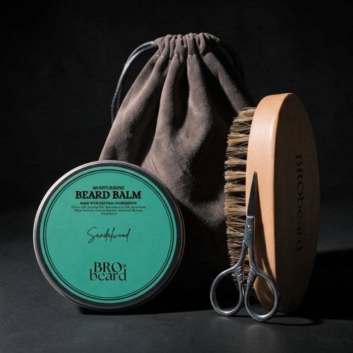 Bro beard beard care set including a round tin of Sandalwood beard balm, a wooden-handled brush, silver scissors, and a dark brown drawstring pouch, arranged on a dark background.